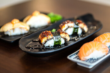 Premium Unagi sushi (Grilled eel) pieces which are served in black plate, placed on wooden table. Japanese food object photo, Close-up and partial focus.