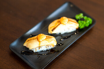Grilled salmon cheese sushi set in black plate which is served on wooden table. Japanese food menu photo. Selective focus at front piece.