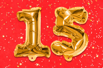 The number of the balloon made of golden foil, the number fifteen on a red background with sequins. Birthday greeting card with inscription 15. Anniversary concept. Celebration event.
