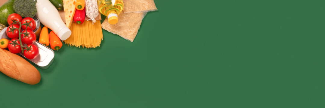 Banner with different groceries, food donations on green background with copy space - pasta, vegatables, canned food, baguette, cooking oil, tomatoes, cheese. Food bank, food delivery concept