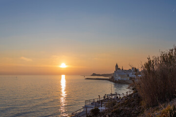 A scenic sunset is reflected in the Mediterranean Sea, with the city of Sitges in the background.