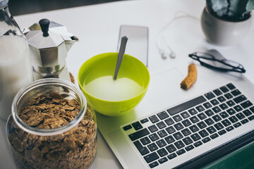 Table set for breakfast, kitchen in the background. Natural meal and technology devices. Interior view of a cozy and modern home. Millennial, youth, home working, home schooling, remote work concept.