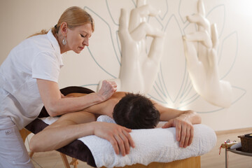 Seniorprofessional masseur working at spa center, massaging back of a man, copy space