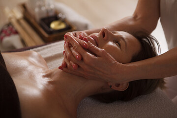 Unrecognizable professional cosmetician doing face massage for mature woman, working at spa center