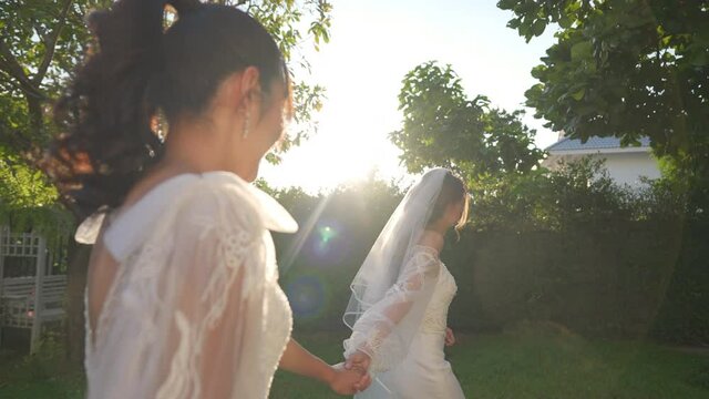 Portrait of Beautiful Asian woman lesbian couple in wedding dress holding hands walking together in the garden. Diversity sexual equality, lgbtq pride, marriage equality and Same-sex marriage concept