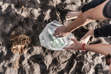 Fototapeta premium Hands of adult man picking up plastics on the beach, collection of polluting waste on the coast, on beaches.