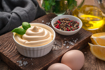 Fresh mayonnaise and ingredients for its preparation on a wooden background. White sauce, homemade mayonnaise.