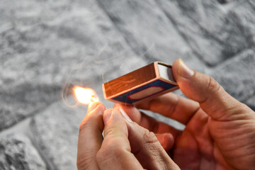 Detail of ignition of matches for a matchbox. A burning match in one hand and a matchbox in the...