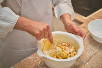 An adult woman in white chef clothes cooking pie in a beige kitchen.