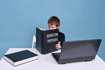 A boy in a school suit with a textbook on quantum physics during distance learning, copy space on a...