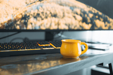 Yellow coffee mug on computer desk and gaming keyboard and monitor in background