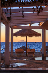 Obraz premium Beach chairs and straw parasol at sunset