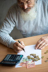 Old bearded senior man with calculator and bills counting euro money and writing notes on white...