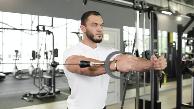 Portrait of professional athlete bodybuilder working out in the indoor gym. Weight lifting and bodybuilding, muscle strengthening workout. Man doing chest exercise with pulley weights. Sport concept.