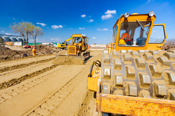 Road roller with spikes and earthmover are working at construction site
