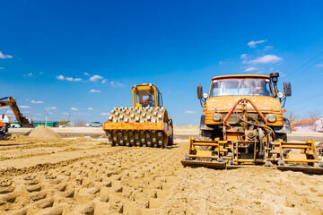 Road roller with spikes and truck plate compactor are working at construction site
