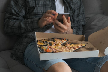 Man is taking photos of pizza in box on his knees using smartphone, closeup view. Unusual pizza...