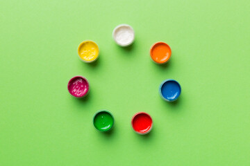 jars with gouache of different colors on Colored background. hobby painting. Top view with empty...