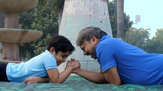 Father and son spending quality time playing in the park - Happy kid  parenting  childhood. A young boy defeating his elderly grandfather in arm wrestling - victorious  leisure time