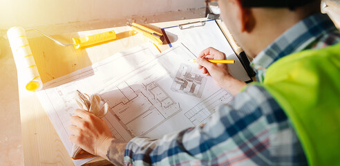 Over the shoulder image of a construction engineer drawing on a sunlit blueprint