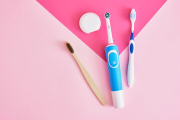 dental floss, electric, bamboo and plastic toothbrushes on a pink background, which brushes are...
