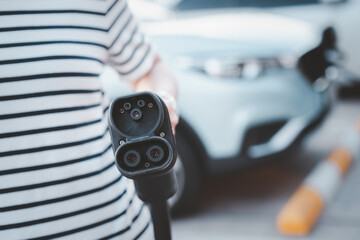 Unrecognizable Asian woman holding a DC - CCS type 2 EV charging connector at EV charging station.