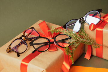 several fashion eye glasses, fir branch and gift boxes with red ribbon on green background copy space