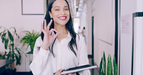 Happy and smiling young businesswoman walking through modern office and showing an okay gesture. Confident young business woman showing 'ok' sign. Female showing success gesture. 