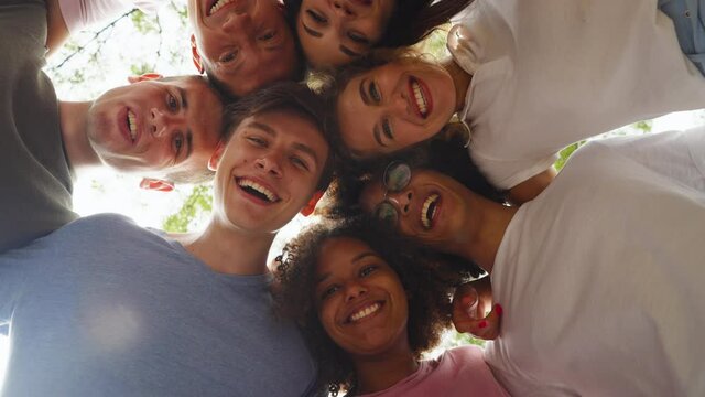 Happy teenagers viewed from below bending over camera, hugging and smiling, trees and sky above them. Concept of friendship