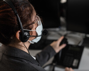 A woman call center operator in a medical mask answers the phone.