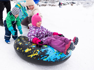 A young woman with children, children 5 and 3 years old, going downhill on an inflatable ring, winter entertainment. A place for winter fun in Finland, skiing down a snow-covered mountain.