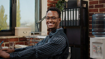 Portrait of african american employee doing commercial work on laptop in startup office. Business...