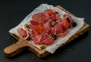 Spanish cold meat assortment. Chorizo, fuet, LOMO, jamon Iberico, olives. Black background. Top view.