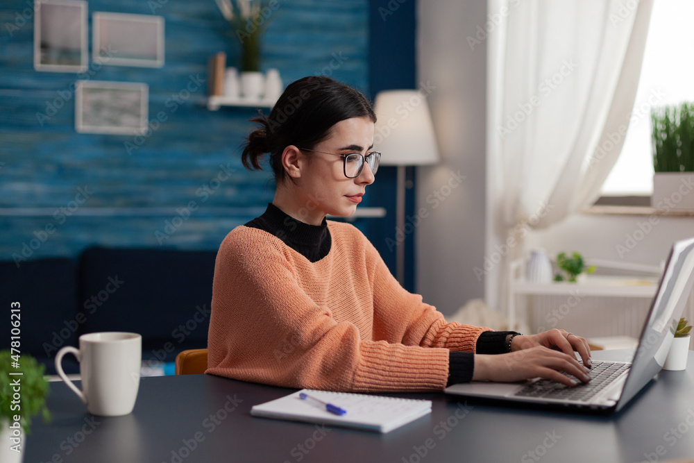 Poster student with glasses typing on laptop sitting at home desk. college girl with notebook studying remo