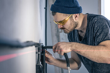 An electrician is mounting electric sockets on the white wall indoors.