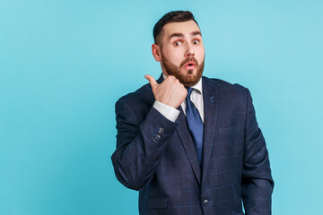Astonished bearded man wearing dark suit pointing finger aside, showing copy space for commercial...