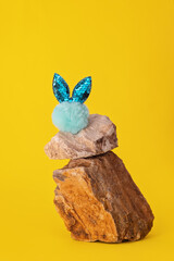 Blue fur easter bunny on a pieces of stone on a yellow background. Trendy Easter still life product photo 