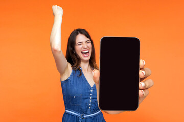 Portrait of happy joyful girl screaming with happiness showing mobile advertisement mockup area and...