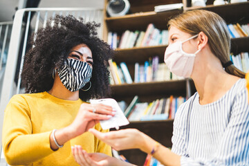Two young female erasmus student respecting anti coronavirus measures while studying at library. Concept of new normal life