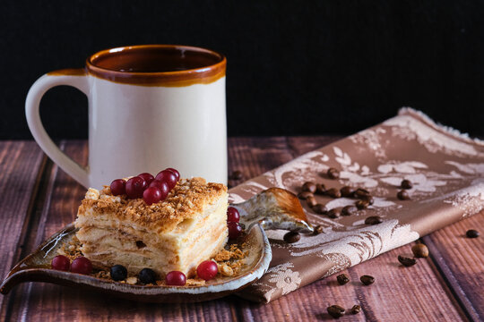 Homemade baked cake Napoleon, Millefeuille. Delicate custard cake garnished with berries. Against the background of a wooden table with a beautiful napkin and whole coffee beans
