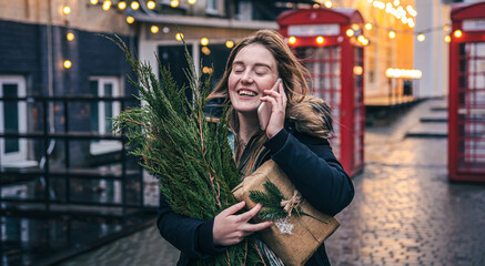 A young woman with a Christmas tree and a gift box talking on the phone.