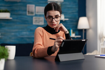 Student with glasses holding stylus touching tablet screen. Programmer in home office interacting...