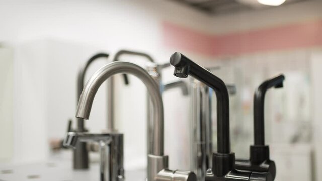 Wide selection of metal and steel faucets standing on counter in hardware store for home repairing and renovations against blurred background