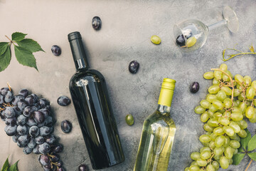 Top view of bottle red and white wine, green vine, wineglass and ripe grape on vintage dark stone table background. Wine shop wine bar winery or wine tasting concept