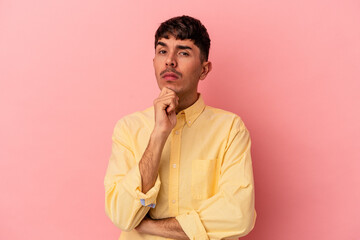 Young mixed race man isolated on pink background suspicious, uncertain, examining you.