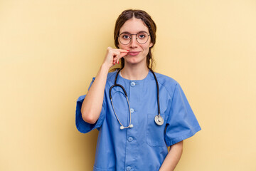 Young nurse caucasian woman isolated on yellow background with fingers on lips keeping a secret.