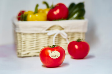 Carbon neutral product label on tomato. Carbon labeling. Basket of vegetables on background. Net zero carbon, emissions free. Organic farm products from local market