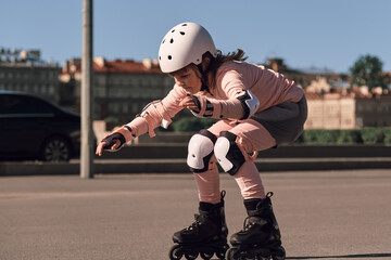 A child of ten is learning to ride rollerblades on city streets. The girl is wearing fall...