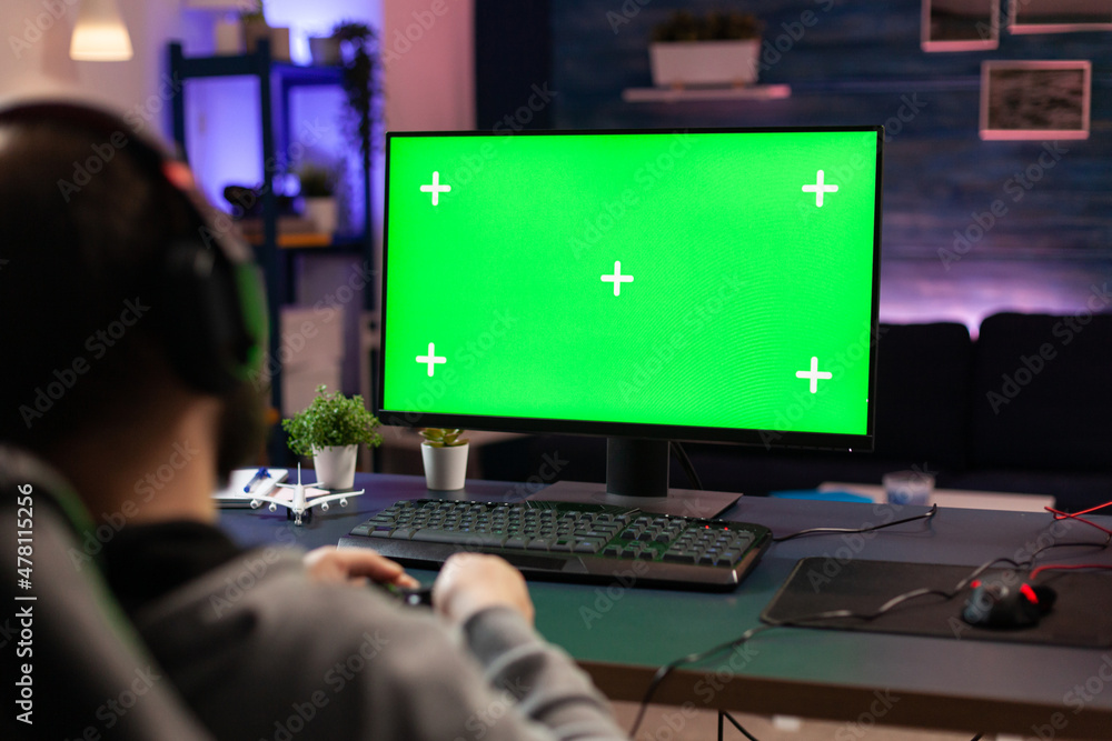 Fototapete gamer using horizontal green screen on computer. man playing video games on chroma key with isolated