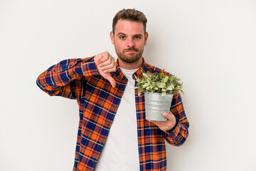 Young caucasian man holding a plant isolated on white background showing a dislike gesture, thumbs...